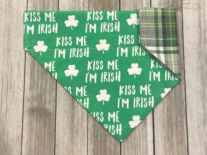 May include: Green dog bandana with white text that reads "Kiss Me I'm Irish" and shamrock graphics. The reverse side features a green, white, and yellow plaid pattern. A festive accessory for St. Patrick's Day.