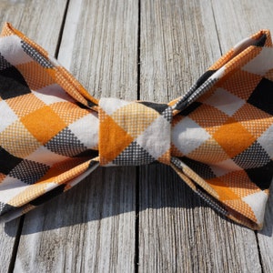 May include: A black, white, and orange plaid bow tie. The bow tie is made of fabric and has a checkered pattern.