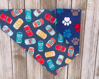 May include: Reversible dog bandana with a navy blue background featuring beer can graphics with phrases like "Woof Brew" and "Fur Buddy." The reverse side has a blue background with paw prints.