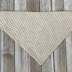 May include: A beige bandana with a brown, small, repeating cross pattern.