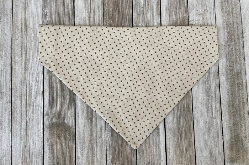 May include: A beige bandana with a brown, small, repeating cross pattern.