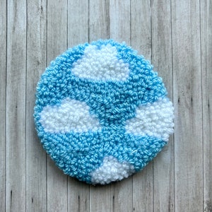 May include: A blue and white round rug with a cloud design. The rug is made of fluffy yarn and has a textured surface.