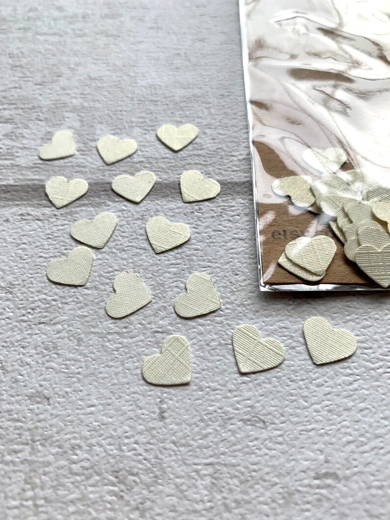 Pode incluir: Um saco de confete de papel branco em forma de cora&ccedil;&atilde;o. Os cora&ccedil;&otilde;es est&atilde;o espalhados sobre uma superf&iacute;cie branca.