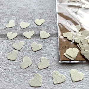 Pode incluir: Um saco de confete de papel branco em forma de cora&ccedil;&atilde;o. Os cora&ccedil;&otilde;es est&atilde;o espalhados sobre uma superf&iacute;cie branca.