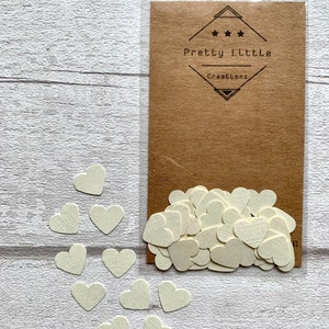 Pode incluir: Um saco de confete de papel branco em forma de cora&ccedil;&atilde;o com um cart&atilde;o marrom que diz "Pretty Little Creations" em texto preto.