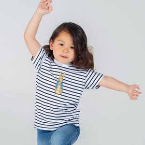 May include: A young child wearing a white and navy blue striped t-shirt with a Peter Rabbit graphic. The child is wearing blue jeans and has their arm raised.