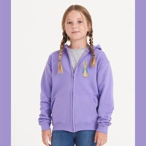 May include: A purple zip-up hoodie with a Peter Rabbit graphic on the front. The hoodie has a hood and a kangaroo pocket.