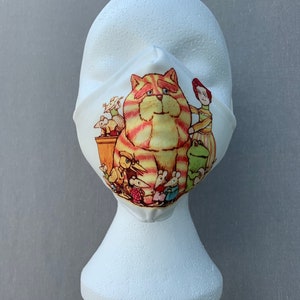 May include: A white face mask with a colorful illustration of a striped cat and several mice. The cat is wearing a hat and the mice are wearing clothes.