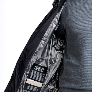 Puede incluir: Chaqueta negra con forro plateado y una etiqueta que dice "SHIELD" con texto sobre el blindaje especial dentro de la tela. El texto menciona que la tela bloquea las radiofrecuencias y las altas frecuencias y es súper efectiva para bloquear la radiación electromagnética.