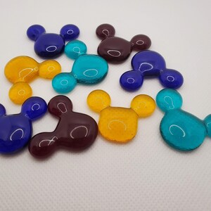 May include: Nine glass Mickey Mouse head shaped ornaments in various colors including blue, teal, yellow, and maroon.