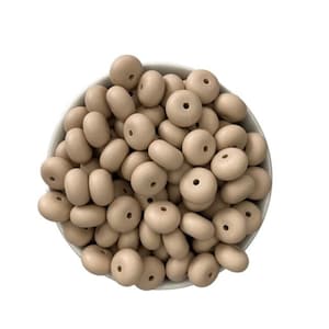 May include: A bowl filled with beige silicone beads. The beads are round with a hole in the center. They are perfect for making necklaces, bracelets, or other crafts.