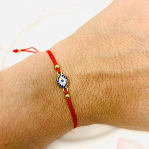 Puede incluir: Pulsera de cuerda roja con un dije de ojo turco dorado. El dije está decorado con piedras azules y blancas.