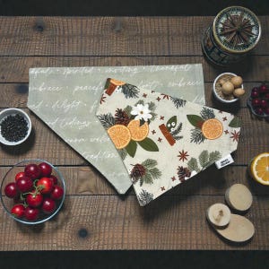 May include: Two decorative bandanas with festive patterns, one with orange slices, pinecones, and cinnamon sticks, the other with holiday-themed words. The bandanas are on a wooden surface with bowls of berries and spices.