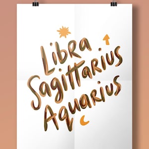 May include: A white rectangular poster featuring the words Libra, Sagittarius, and Aquarius written in a brown and tan script font. The design includes a small yellow star icon above the text and a yellow crescent moon icon below the text.