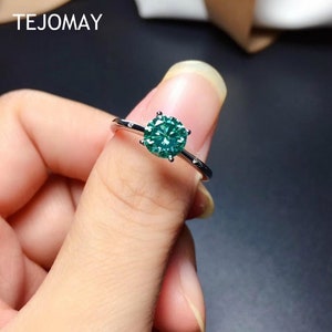 May include: A silver ring with a green gemstone set in a prong setting. The ring is on a finger.