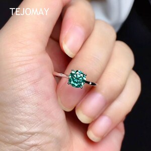 May include: A silver ring with a round, green gemstone set in a prong setting. The ring has two small accent stones on the band.