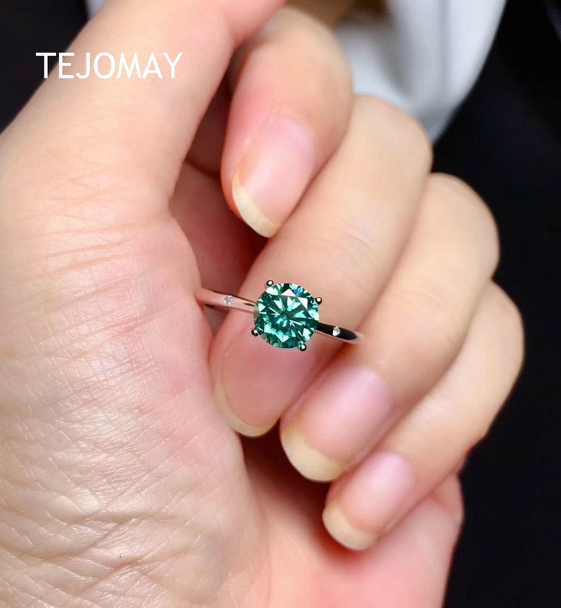 May include: A silver ring with a round, green gemstone set in a prong setting. The ring has two small accent stones on the band.