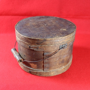 May include: A wooden bucket with a metal handle and a wooden lid. The bucket is brown and has a worn finish.