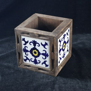 Puede incluir: Una caja de madera con un diseño de azulejos azul y blanco. El azulejo presenta un centro amarillo con un patrón floral azul y blanco.