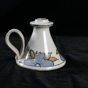 May include: A white ceramic candle holder with a blue and yellow floral design and a handle.