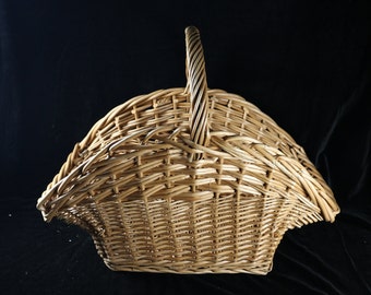 May include: A natural woven wicker basket with a handle. The basket is shaped like a half-circle and has a wide opening.