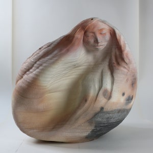 May include: A ceramic sculpture of a woman's head and shoulders, with her hair flowing around her. The sculpture is made in a light brown and white color with black accents.