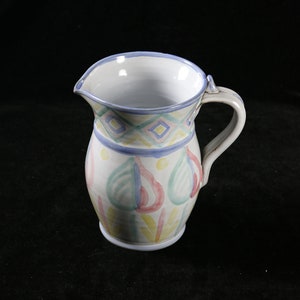 May include: A white ceramic pitcher with a blue rim and a colorful hand-painted design of green, pink, and yellow pears.