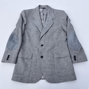 May include: A gray tweed blazer with gray suede elbow patches. The blazer has two front pockets, three buttons on each cuff, and two buttons down the front. The interior lining is a light gray color.