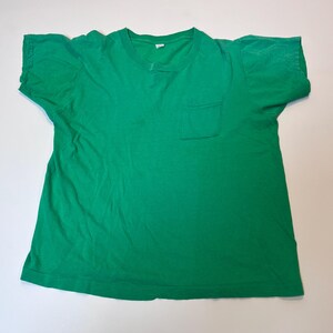 May include: A solid green t-shirt with a crew neck and a single pocket on the left chest. The shirt is made of a soft material and has short sleeves. The t-shirt is laid flat on a white surface.