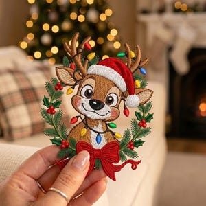 May include: An embroidered patch featuring a cartoon reindeer wearing a red Santa hat, surrounded by a wreath of green pine needles, red berries, and colourful Christmas lights, finished with a large red bow at the bottom of the design.