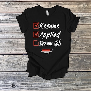 Puede incluir: Camiseta negra con una lista de verificación blanca que dice "Currículum", "Solicitado" y "Trabajo de ensueño". Una barra de progreso roja debajo de la lista de verificación dice "cargando..."