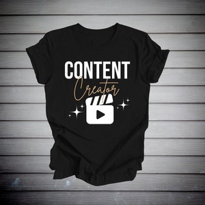 May include: Black t-shirt with white text that reads "CONTENT creator" and a white film clapboard with a play button inside. The text "creator" is in a gold cursive font. There are two gold stars on either side of the clapboard.