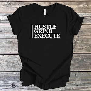 May include: Black t-shirt with white text that reads "Hustle Grind Execute"