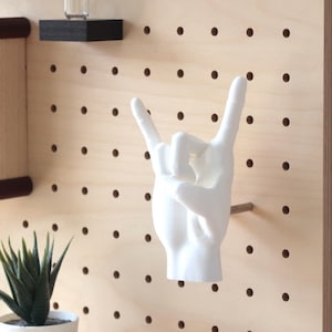 Peut inclure: Main en céramique blanche en forme de geste de rock and roll montée sur un mur en panneau perforé.