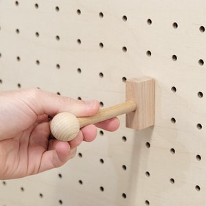 May include: A wooden peg with a round knob on one end and a rectangular block on the other end. The peg is inserted into a pegboard.