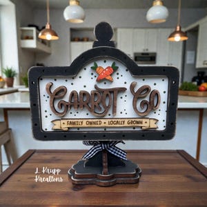 May include: A decorative wooden sign featuring a black frame and a white background with black polka dots. The sign displays the text "CARROT CO" in large brown letters, with a small carrot icon above and a banner reading "FAMILY OWNED - LOCALLY GROWN".