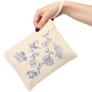 May include: A beige canvas zippered pouch with a blue floral design and the words "faith", "hope", "charity", "prudence", "fortitude", "temperance", "justice" printed on it.