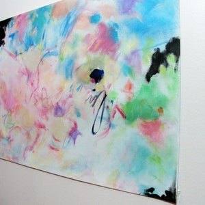 May include: Abstract painting with a vibrant mix of colors including blue, pink, green, and purple. The artwork features brushstrokes and splatters, with black accents at the corners. The painting is mounted on a white surface.