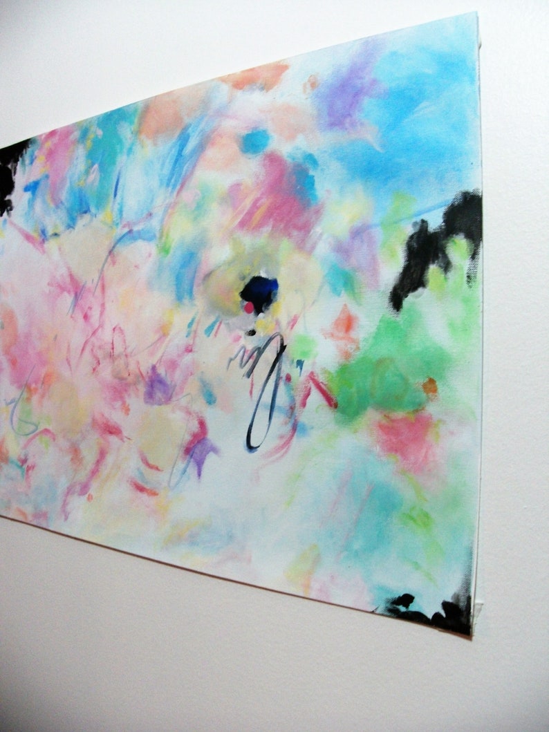 May include: Abstract painting with a vibrant mix of colors including blue, pink, green, and purple. The artwork features brushstrokes and splatters, with black accents at the corners. The painting is mounted on a white surface.