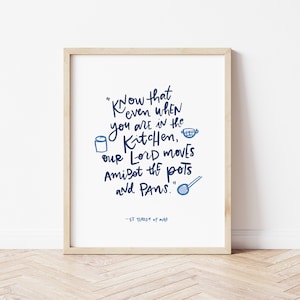 Puede incluir: Una impresión enmarcada con una cita azul y blanca que dice "Sepa que incluso cuando está en la cocina, nuestro Señor se mueve en medio de las ollas y las sartenes." La cita se atribuye a "Santa Teresa de Ávila".