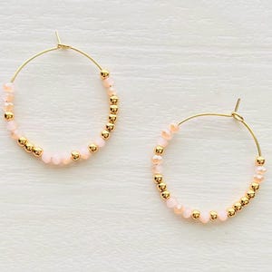May include: Gold hoop earrings with pink beads. The earrings are made with small gold beads and larger pink beads.