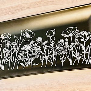 May include: A rectangular black ceramic tray with a white floral design. The tray features a glossy finish and a border of white flowers and foliage. The design is a continuous line drawing of various wildflowers.