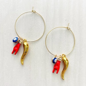 May include: Gold hoop earrings with red chili pepper and blue evil eye charms.