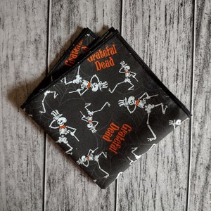 May include: Black cotton handkerchief with a repeating pattern of skeletons dancing and the words "Grateful Dead" in orange.
