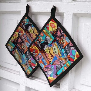 Puede incluir: Dos agarraderas cuadradas con borde negro y un diseño de collage colorido con personajes y texto de "The Mandalorian". Las agarraderas tienen un lazo para colgar.