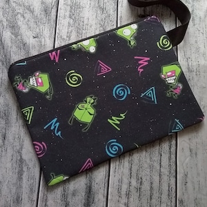 May include: Black zippered pouch with a green alien character print. The pouch has a black strap and a zipper closure.