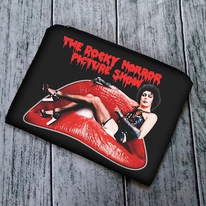 Puede incluir: Bolsa negra con cremallera con una imagen roja y blanca de un personaje de la película "The Rocky Horror Picture Show".