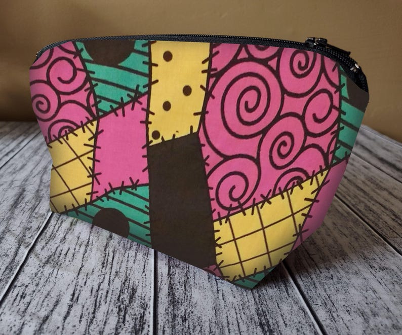 Pu&ograve; includere: Una trousse da trucco in stile patchwork rosa, verde, giallo e nero con chiusura a zip. La borsa ha un design cucito fantasioso.
