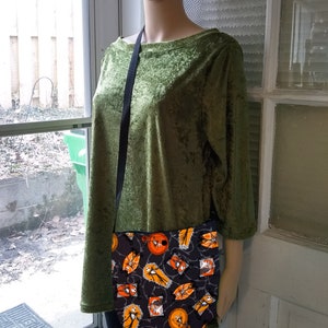 K&ouml;nnte beinhalten: Eine schwarze Umh&auml;ngetasche mit einem Halloween-Motiv, das orangefarbene und wei&szlig;e Jack-Skellington-Figuren auf schwarzem Hintergrund zeigt.