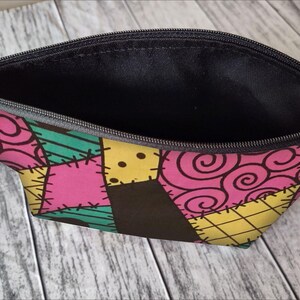 Pu&ograve; includere: Una pochette nera con cerniera con un design a patchwork che presenta tessuto rosa, giallo, verde e marrone. Il tessuto ha un motivo cucito e un design a spirale.